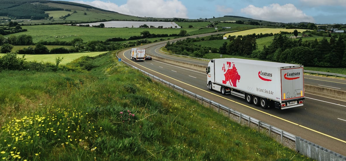 Vrachtwagen van Leatrans op een snelweg door groene heuvels