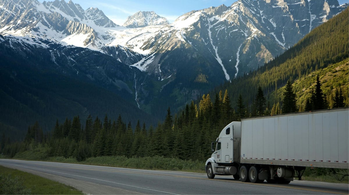 Truck on a road below snow-capped mountains