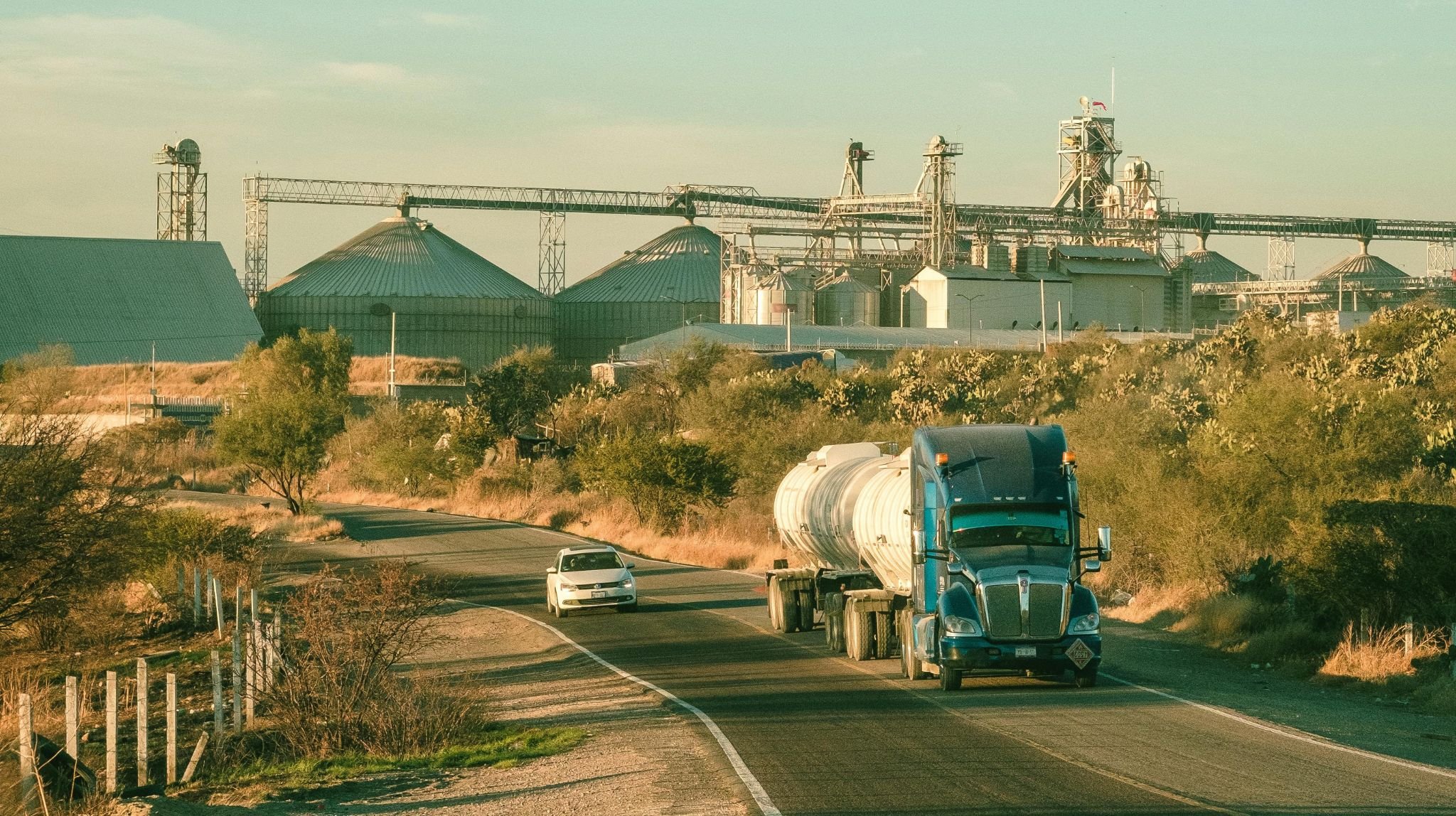 Tanker truck on a road past grain silos