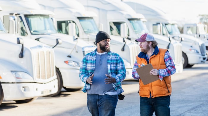 Two drivers talking in front of a row of trucks