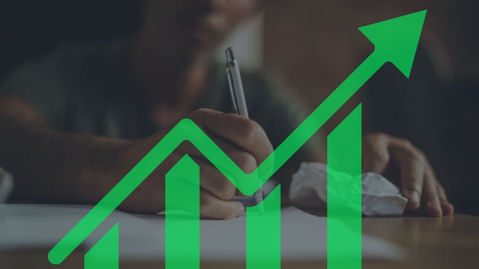 Person writing with a rising chart overlay