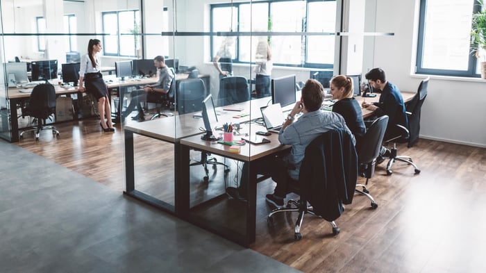 Planning teams working at separate desks in an open-plan office with glass partitions